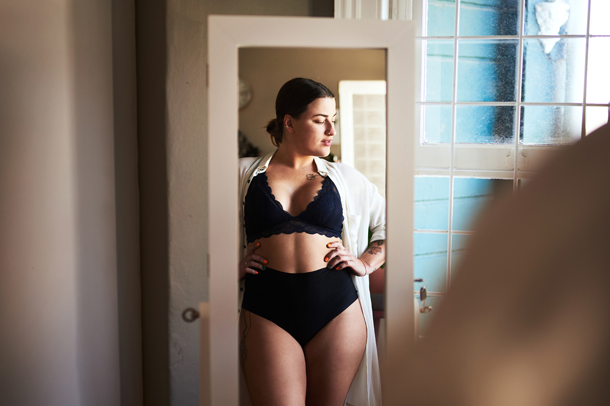 a woman standing in her bra and underwear looking at a mirror after getting a breast lift in Bellevue, WA